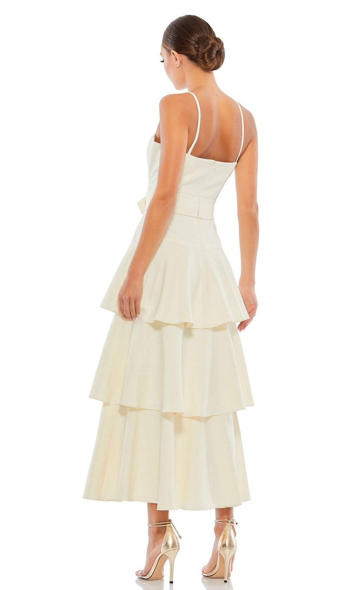 A woman in the Short Wedding Guest Dress 26629 by Mac Duggal, featuring a cream ruffle-layered design with thin straps and a tiered skirt, stands in profile with her back to the camera, paired with high-heeled sandals.